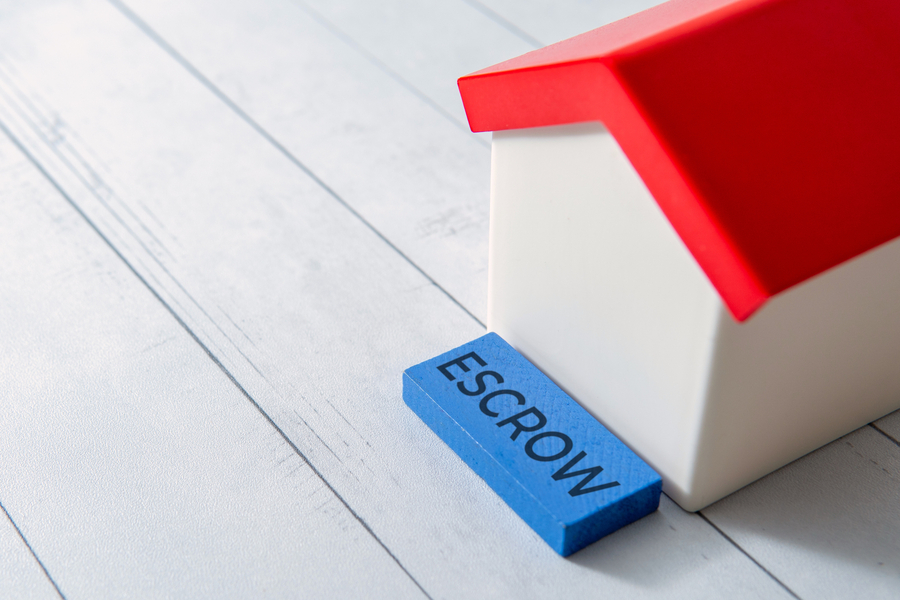 The word ESCROW next to a small toy house. Real estate transactions or financial security concept.