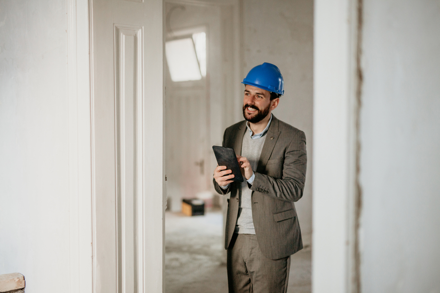 A photo of a handsome architect with a beard, wearing a gray suit and a blue protective helmet